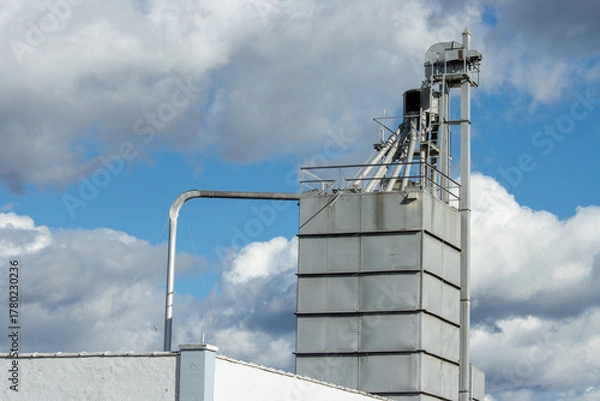 Fototapeta Feed mill equipment against a cloudy sky