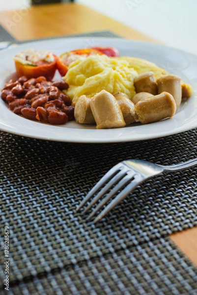 Fototapeta Hotel healthy breakfast menu of mashed potatoes, omelette, read beans, tomatoes, and sausages served on a white plate