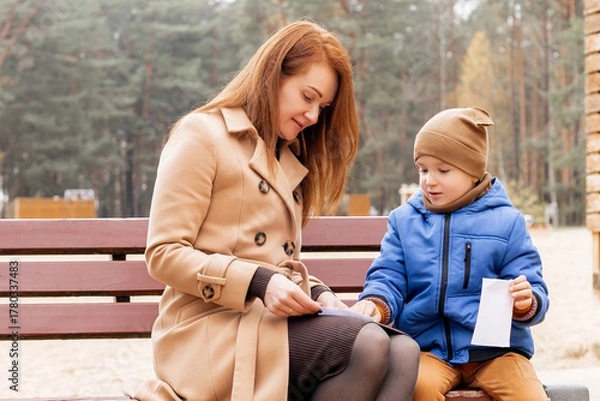 Fototapeta Mother and Son Folding Paper Boat Together on Park Bench During Autumn Day