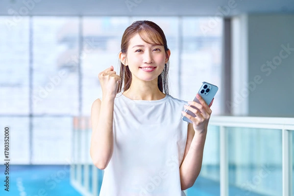 Obraz ジムでトレーニングしてスマホを見て喜ぶ女性　撮影協力：スポーツクラブ&サウナスパ ルネサンス 幕張24
