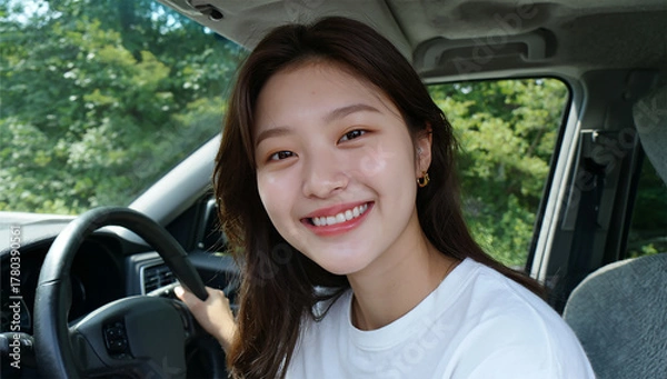 Fototapeta A young woman sitting inside a car looking thoughtfully outside with lush green nature visible through the window.