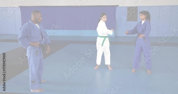 Fototapeta Directing instructor in blue gi guiding students sparring in dojo on foam mats, with colored belts