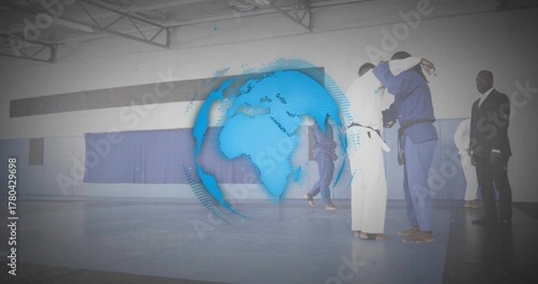 Fototapeta Grappling pair of martial artists practicing judo on blue mats at gymnasium, with digital globe