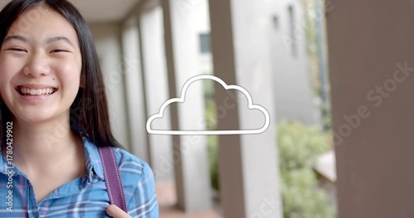 Fototapeta Smiling schoolgirl wearing blue shirt with backpack strap in campus walkway, cloud icon, copy space
