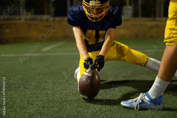 Obraz American football player holding ball on field at night