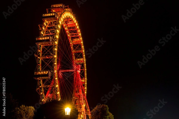 Fototapeta Ferris Wheel Illuminated at Night with Vibrant Red and Yellow Lights