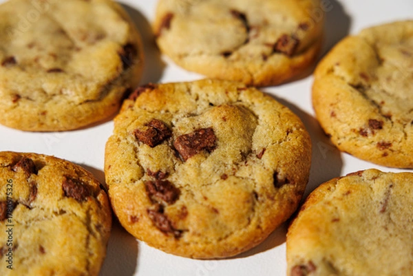 Fototapeta A detailed view of golden brown chocolate chip cookies arranged on a white surface, showing melty chips and soft texture under natural light. No visible branding