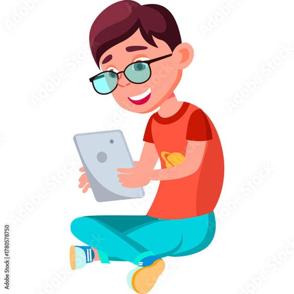 Fototapeta Young Boy with Glasses Enthusiastically Using a Tablet Computer Sitting Cross-legged in Casual Attire with a Blue Background