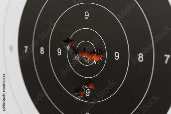 Fototapeta Macro close-up of multiple bullet holes impacting the center bullseye of a paper shooting target, showing high accuracy.