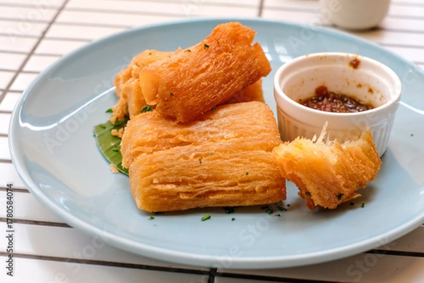 Fototapeta Golden fried cassava served on a light blue plate with white background. Perfect for restaurant menu design, tropical food promotion, or culinary asia traditional snacks.