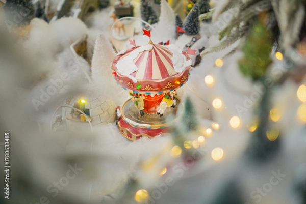 Fototapeta miniature Christmas carousel covered in fake snow with soft bokeh lights in a winter village display concept of holiday decoration, festive retail, seasonal entertainment