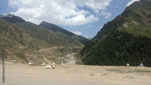 Fototapeta Scenic mountain landscape with winding road and sparse settlements under a vast sky.