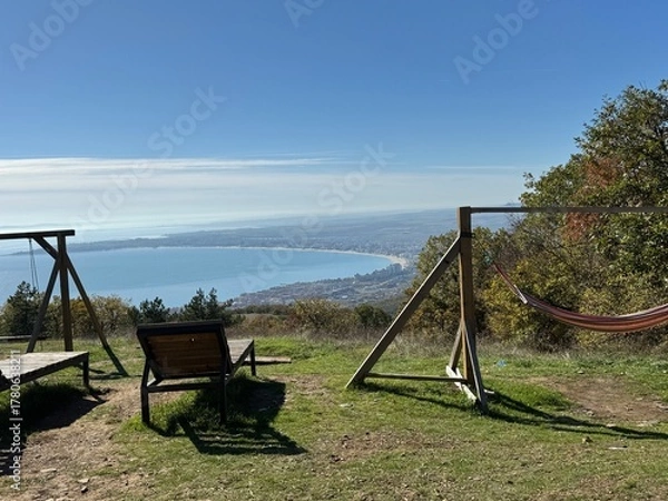 Fototapeta playground in the forest Beautiful scenic view with a wooden swing and bench overlooking the calm blue sea on a sunny day. Peaceful coastal landscape and clear sky. Perfect travel and relaxation conce