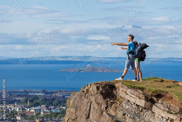 Fototapeta Two hikers marvel at expansive views from a grassy cliff edge