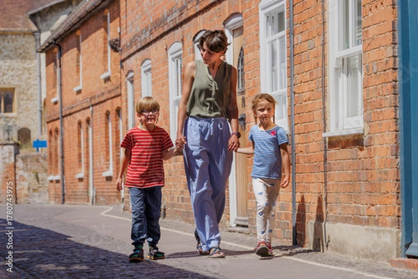 Fototapeta Woman walking with two kids by brick buildings in Farnham, UK