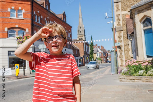 Fototapeta Happy boy shades eyes in sunny town street, red striped shirt