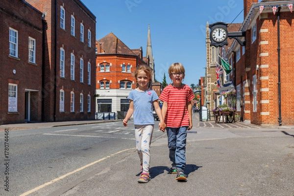 Fototapeta Two kids hold hands, walking down a sunny street of Farnham, UK