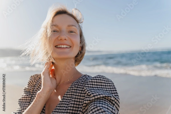 Fototapeta Portrait of happy young woman enjoying fresh air on the beach. Beautiful smiling female having fun on the ocean. Concept freedom and carefree vacation. Beach Holidays.