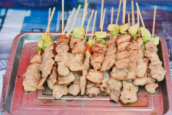 Obraz Grilled pork skewers on a tray, some with vegetables.