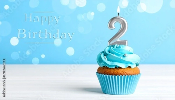 Fototapeta Delicious blue frosted cupcake with a lit silver number two candle, perfect for a second birthday celebration against a sparkling bokeh background, symbolizing joy and milestones