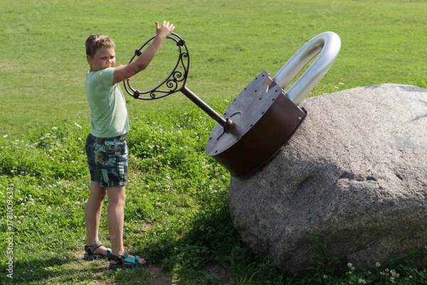 Fototapeta A boy and a gigantic lock with a large metal key in the park.