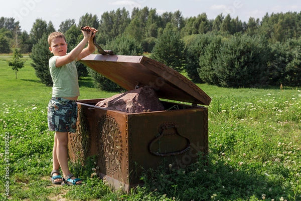 Fototapeta A little boy opens a large metal chest and finds a large stone inside