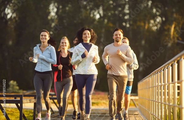 Fototapeta Sporty happy group of friends running together along outdoor track exercising for fitness activity showing health and friendship, shared enjoyment, jogging sport team, pace, movement work out