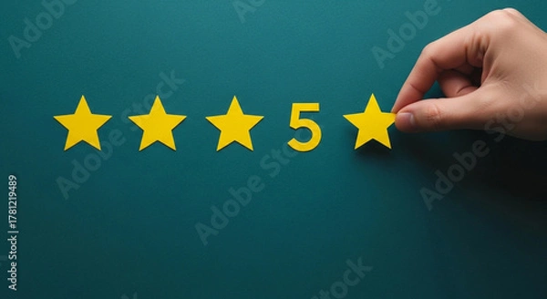 Fototapeta Hand placing the final yellow star to complete a five star rating on a dark green background