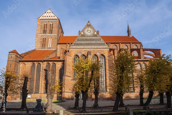 Fototapeta St. Nicholas Church in sunshine, with red roofs, tall windows, and autumnal trees in the foreground