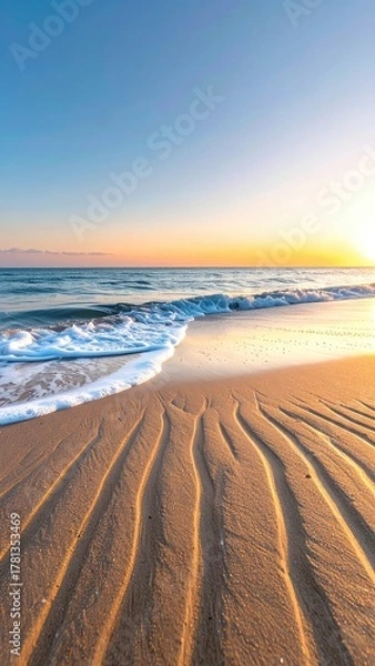 Fototapeta Golden sunrise over a tranquil ocean with rippled sand and gentle waves