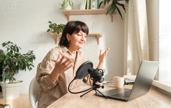 Obraz Mature caucasian female podcaster engaging in online discussion with laptop and microphone setup