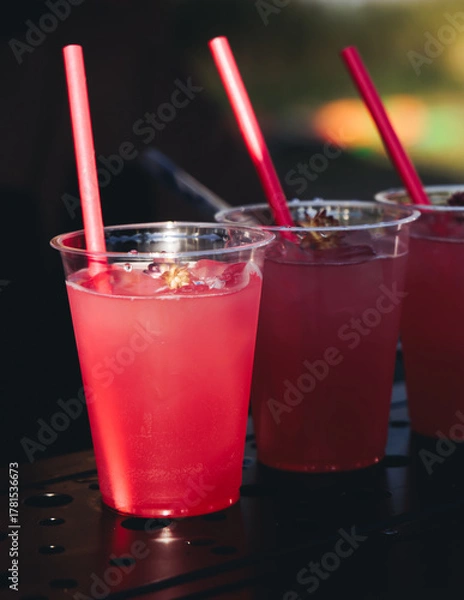 Fototapeta Barman mixing liquor beverages and alcohol drinks in plastic cups, bartender working, beautiful row line of different coloured cocktails on open air summer party in a bar, catering on banquet event