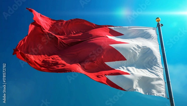 Fototapeta Bahrain's vibrant national flag waves proudly against a crystal clear blue sky, a symbol of freedom, unity, and national pride on a bright sunny day