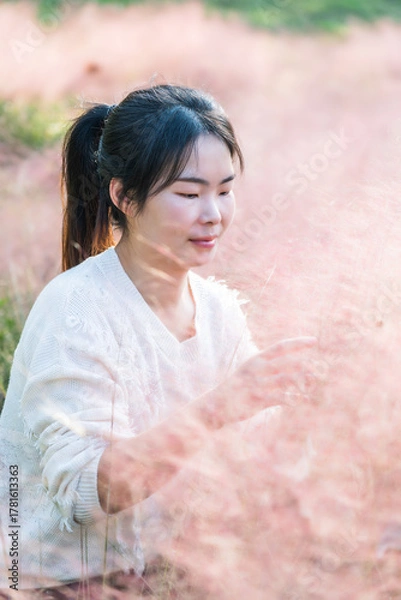 Fototapeta Woman enjoying the pink muhly grass in a field