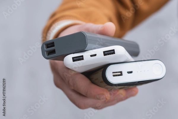 Fototapeta Close-up of a person holding several portable power banks in hand. Modern charging technology, multiple USB ports and battery indicators for energy on the go.