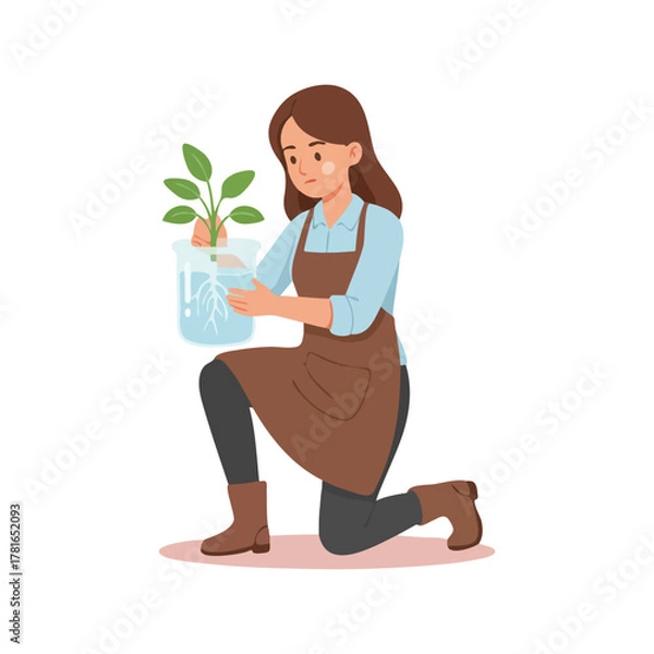 Obraz Young woman in apron kneeling holding a small plant in a clear container.