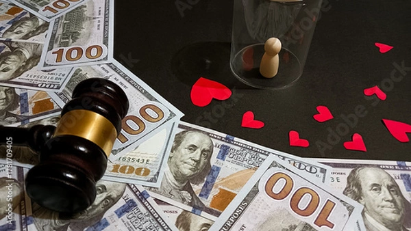 Fototapeta A symbolic composition showing a gavel, dollar bills, a wooden figure under glass, and red hearts, representing the balance between love, money, and justice in human relationships.