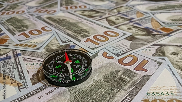 Fototapeta A compass placed on a spread of hundred-dollar bills, symbolizing time, wealth, and guidance in financial decisions and investment strategies.