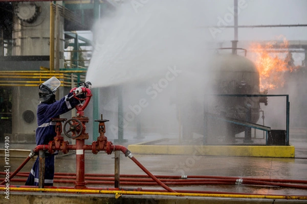 Fototapeta Firemen using water from hose for fire fighting at firefight training of insurance group. Firefighter wearing a fire suit for safety under the danger case.