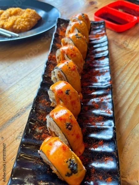 Obraz Fresh sushi rolls with spicy orange sauce served on black plate. A modern Japanese cuisine presentation symbolizing luxury, flavor, and the art of traditional culinary craftsmanship.