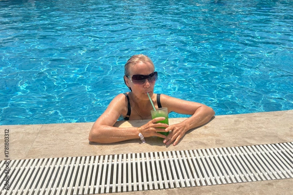 Fototapeta A retired woman enjoys a cold lemonade in the pool