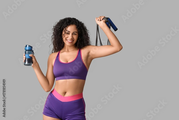 Fototapeta Sporty young African-American female coach with jumping rope and water bottle on white background