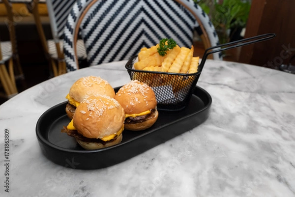 Fototapeta Mini burgers and french fries are a classic meal. The mini burgers are arranged in a row next to a serving of golden french fries. These delicious and tasty food sit on a stylish dark tray