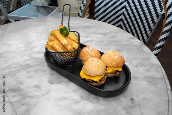 Fototapeta Delicious mini burgers with fries on a table. The image shows mini burgers with cheese and fries on a plate 