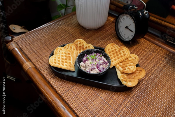 Fototapeta Heart-shaped waffles and a small dish filled with dip, a clock, and a potted plant are on a table