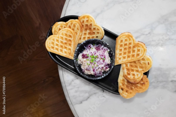Fototapeta Heart-shaped waffles and dip, arranged for a delicious treat on a black serving plate. They symbolize love and enjoyment