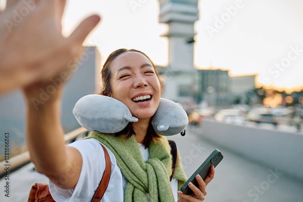 Obraz Smiling Asian woman traveling, wearing a neck pillow and scarf, doing a high five, ready to go