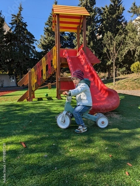 Fototapeta Happy toddler on a balance bike exploring a colorful playground on a crisp autumn day.

