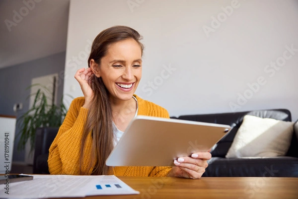 Fototapeta Cheerful woman at her apartment using digital tablet