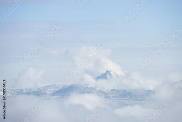 Obraz Snowy mountain peak surrounded by white fluffy clouds